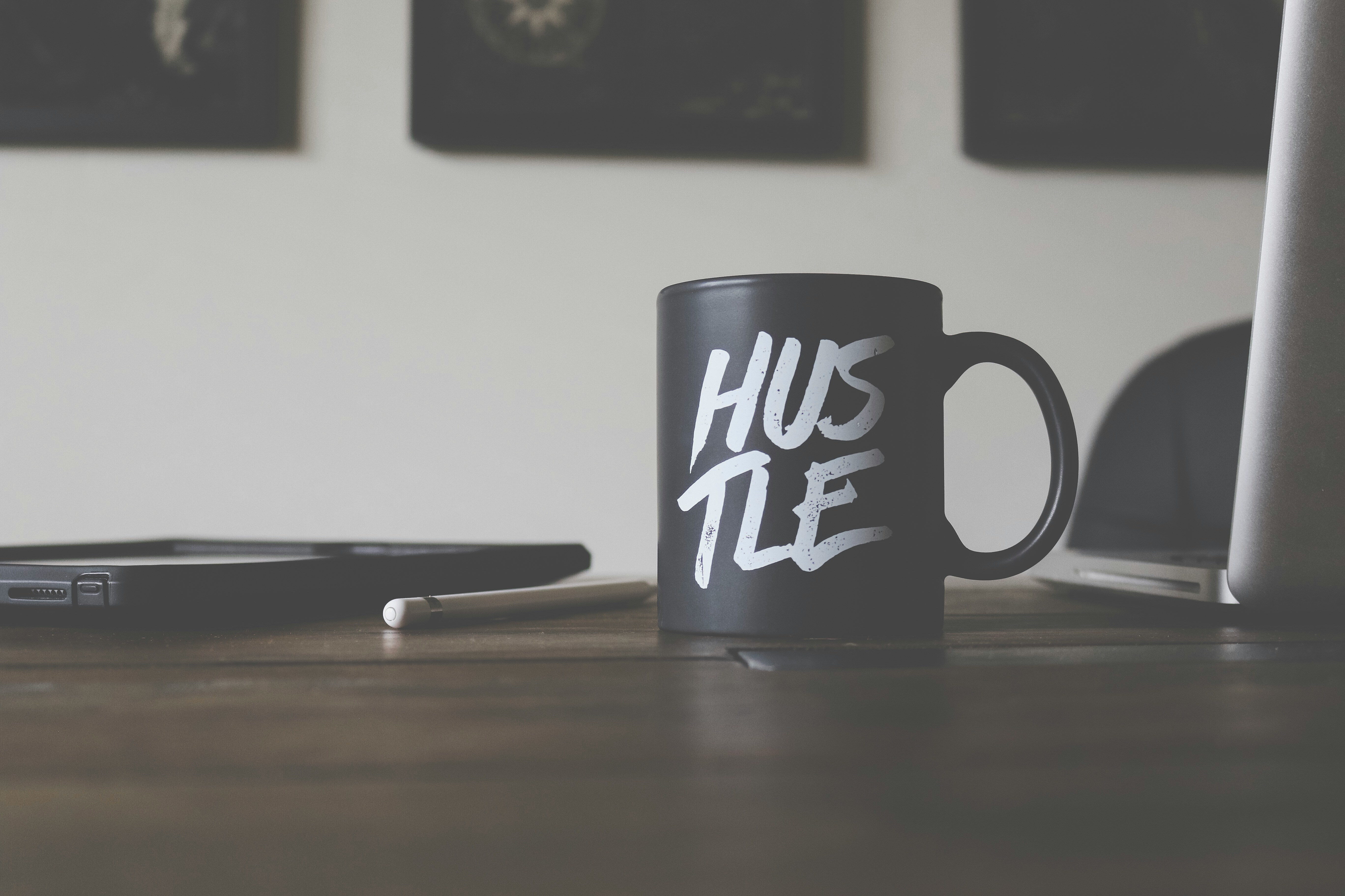 A motivational workspace featuring a black cup with the word ‘hustle’ in white, a laptop, pen, and phone, creating an inspiring atmosphere for productivity.